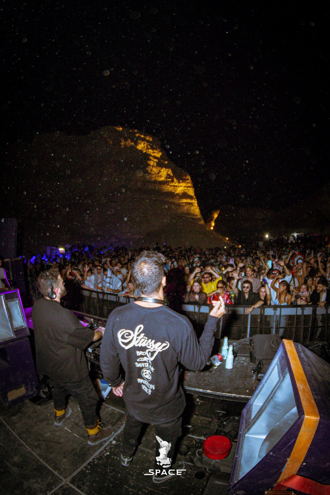SPACE crowd dancing at night beneath a mountain ridge and a starry sky
